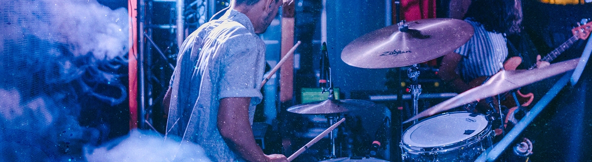 Man playing the drums in blue light amongst smoke on stage.