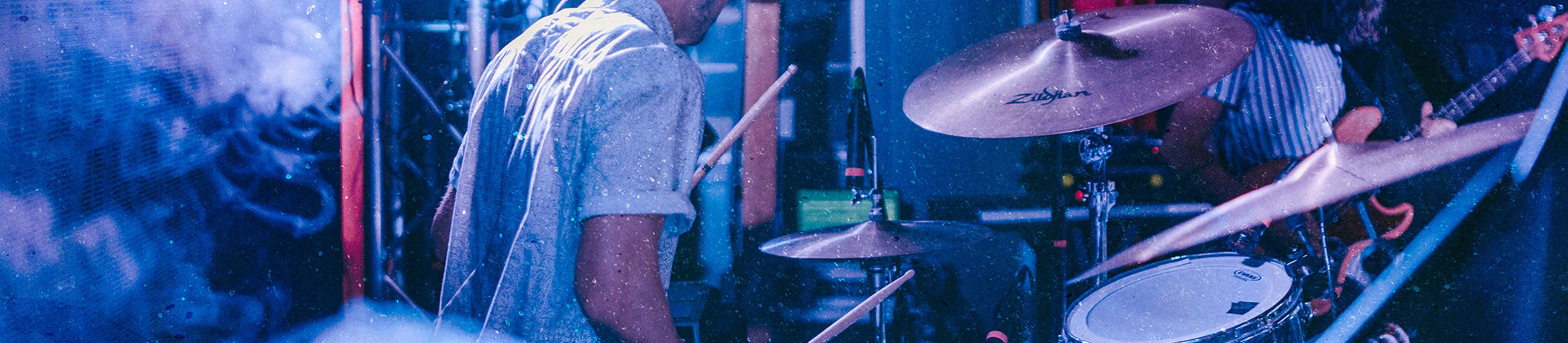 Man playing the drums in blue light amongst smoke on stage.