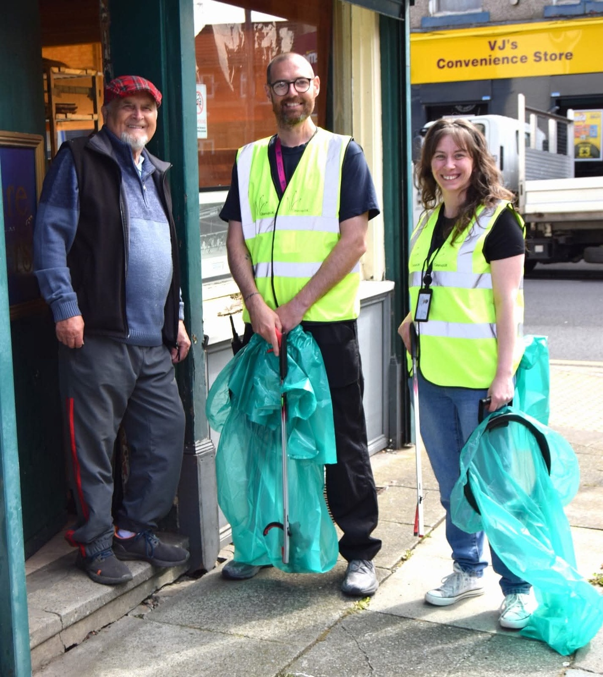 3 adults conduct litter picking in a town centre, two wearing high vis vest