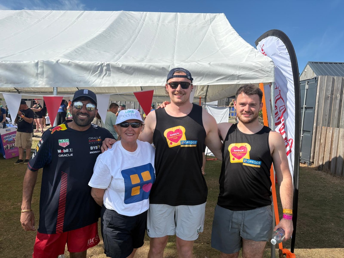 3 men in black vests stand with a women in a white greggs foundation t-shirt in front of a gazebo
