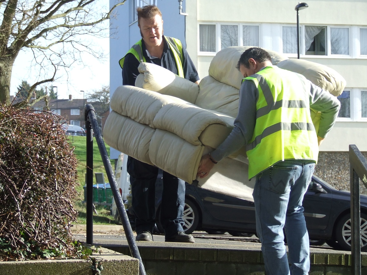 2 men lift a sofa down some stairs outdoors