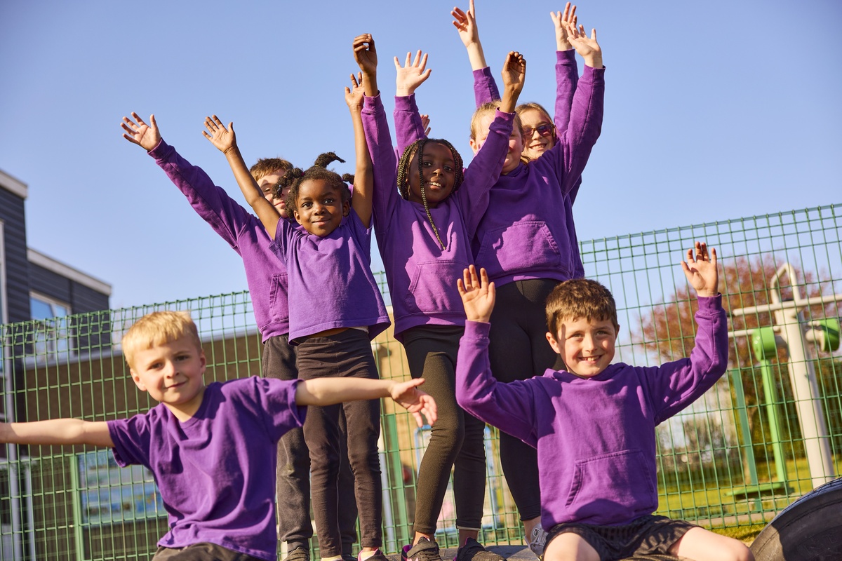 a group of children in purple tshirts hold up their hands