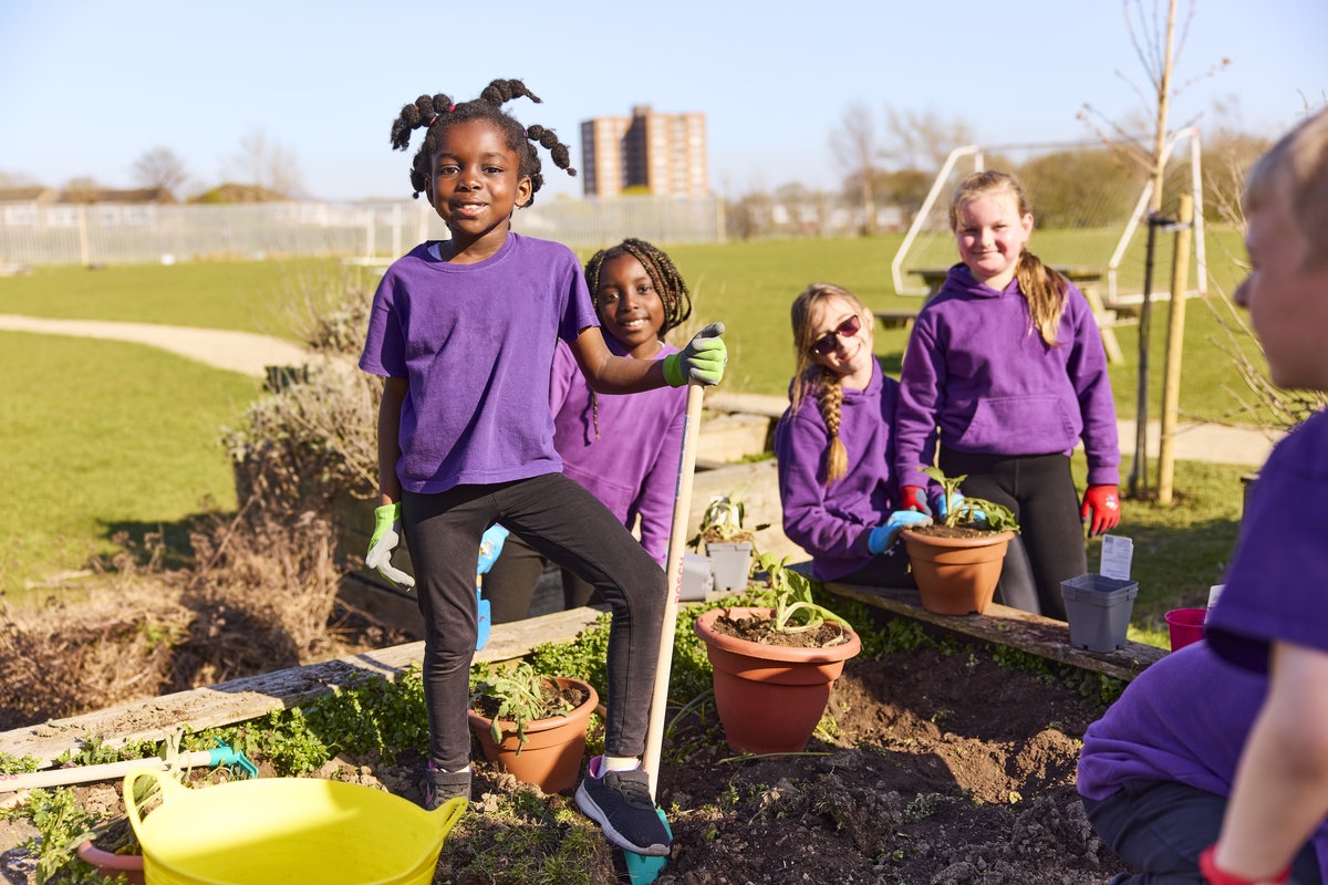 Children in purple shirts gardening, smiling together in a sunny garden.