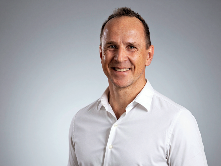 Man smiling in a white shirt against a neutral gray background.
