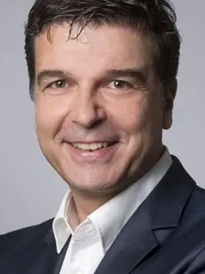 Smiling man in a suit with short dark hair and a light gray background.