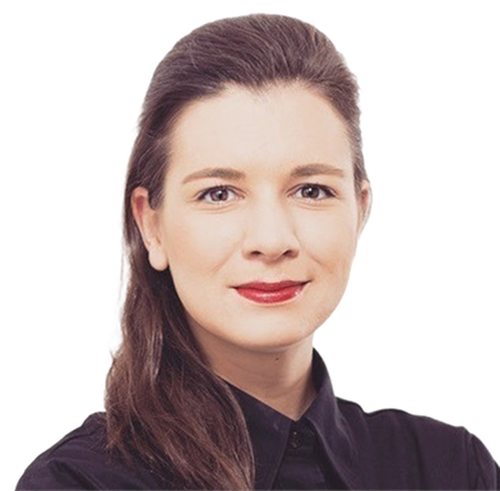 A woman with brown hair and red lipstick, wearing a black shirt, smiles at the camera against a plain background.