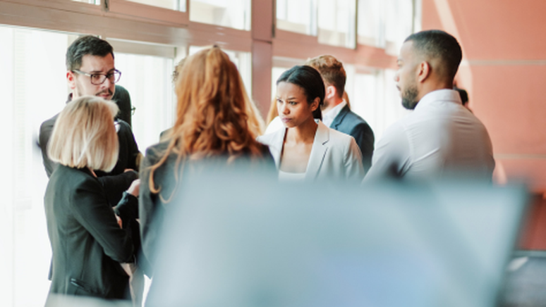 A group of professionals in formal attire engaged in a serious discussion near large windows in an office setting.