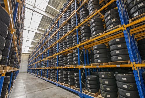 Rows of stacked tires on metal shelves in a large warehouse with high ceilings and skylights.