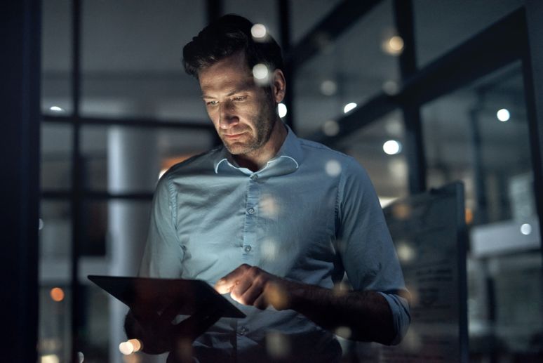 Geschäftsmann im dunklen Büro am Tablet