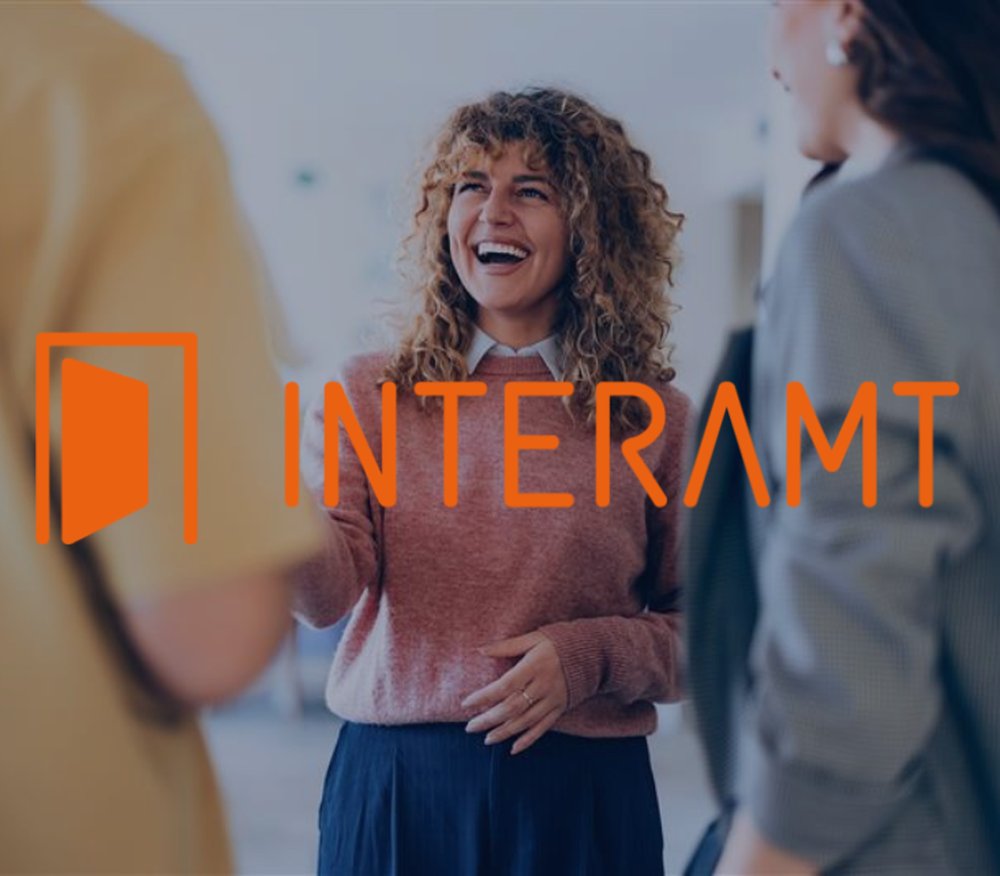 Woman smiling and interacting with two people, standing together, with "INTERAMT" logo overlayed in bright orange.