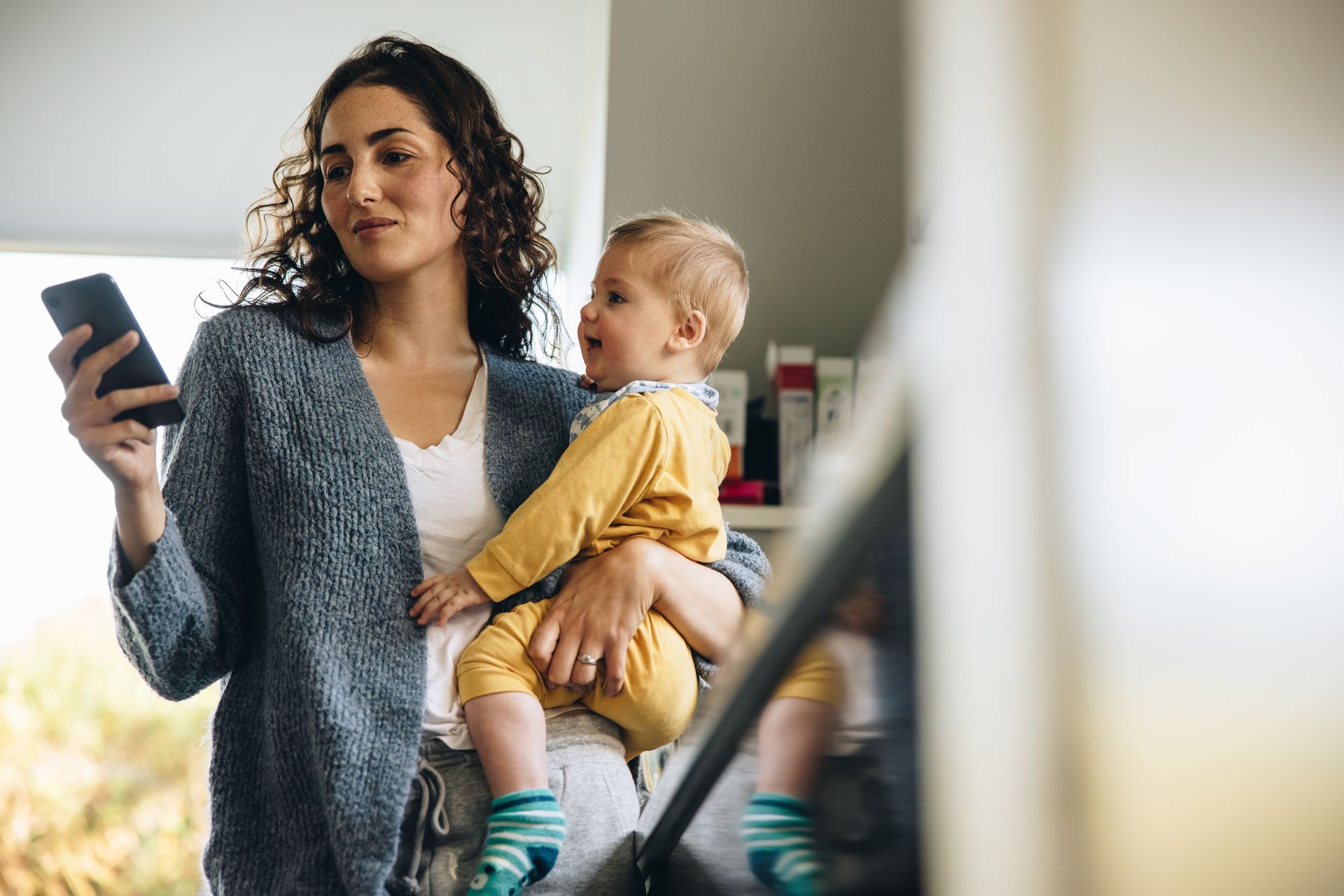 Mutter mit Baby auf dem Arm und Smartphone in der Hand