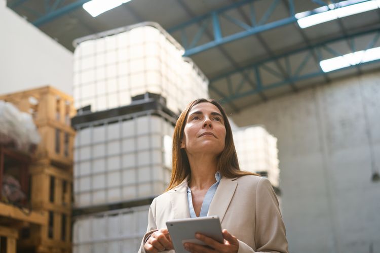 Mature businesswoman with digital tablet standing in warehouse. Woman manager checking inventory of products in distribution warehouse
