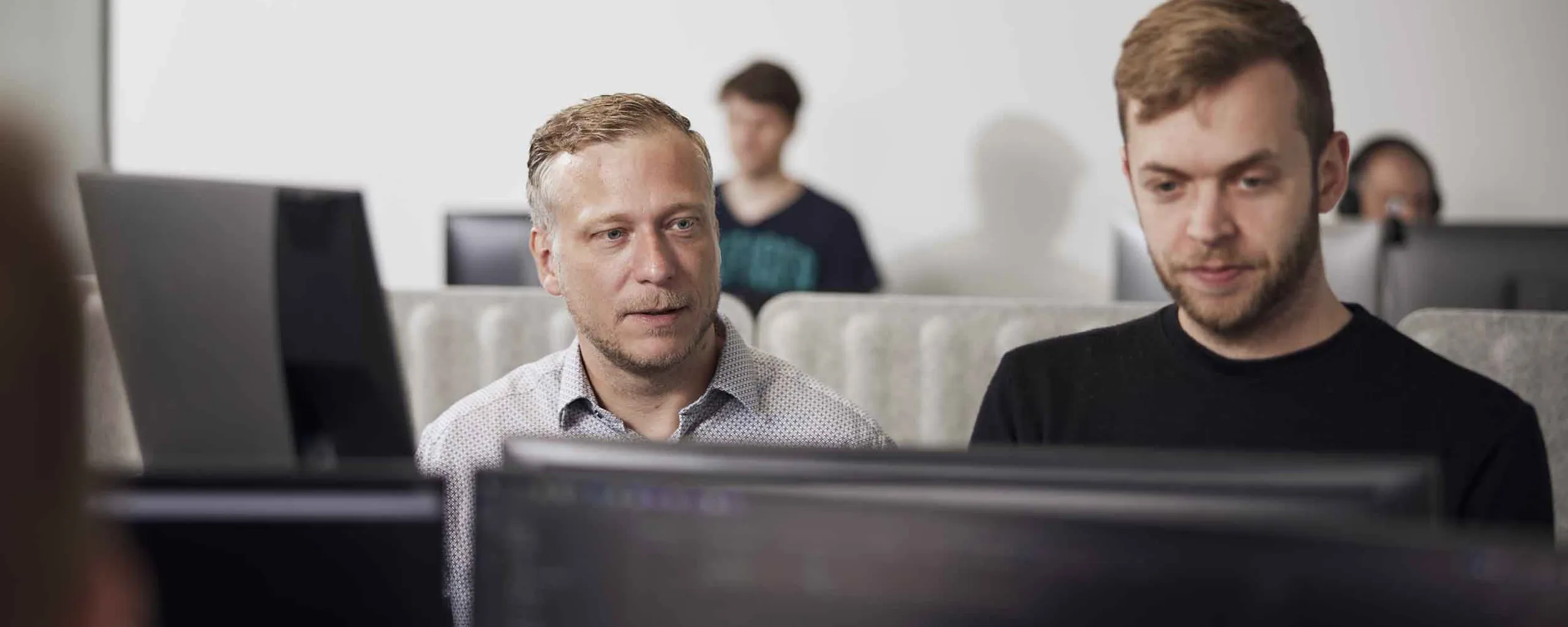 To webudviklere sidder ved hver sin computerskærm og samarbejder.
