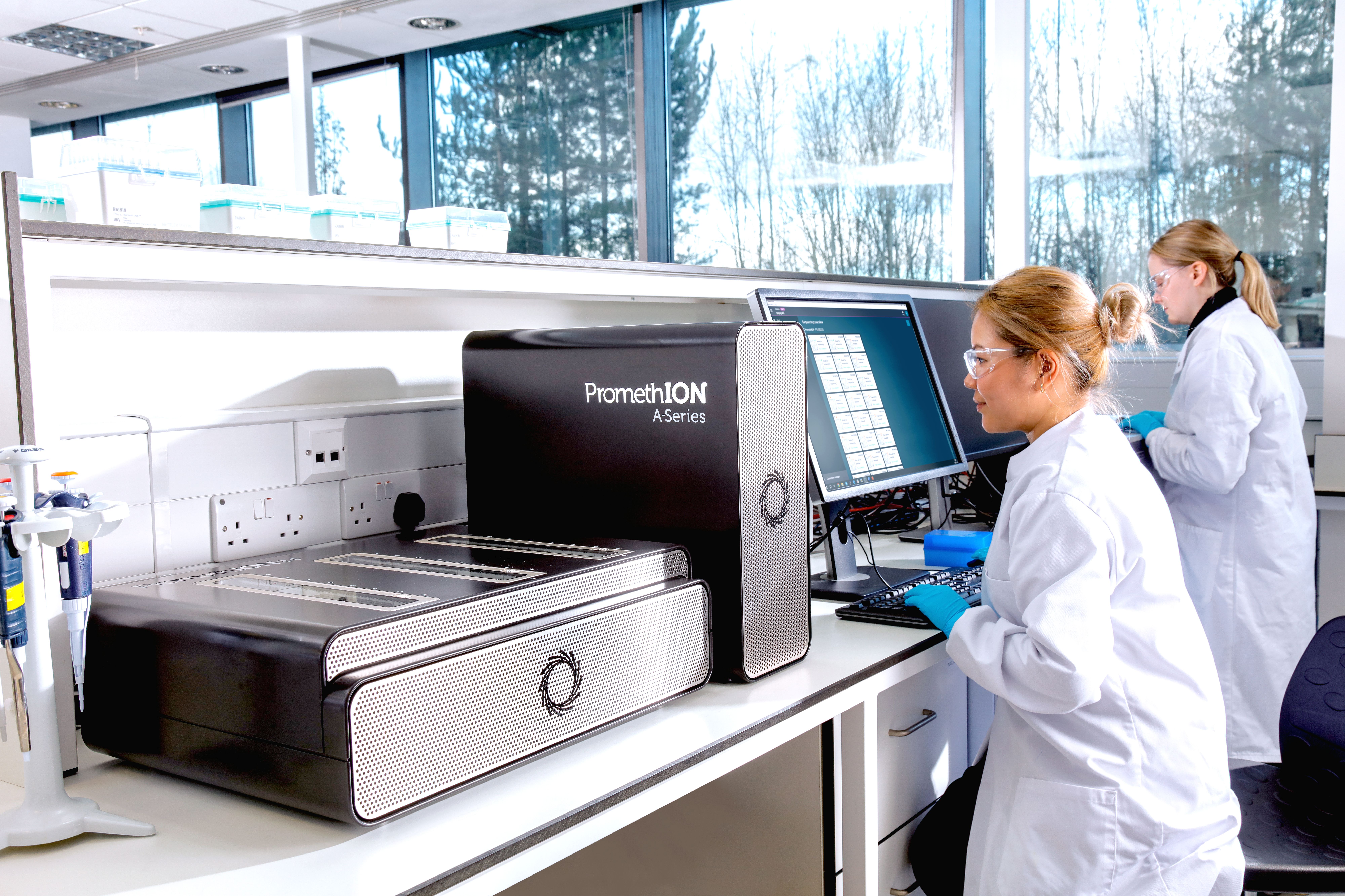 Image of a PromethION 24 in the lab next to two scientists