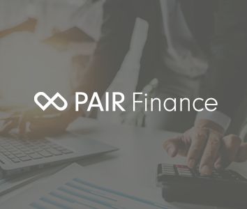 A blurred image with a person using a calculator near a laptop, overlaid with the logo and name "PAIR Finance."