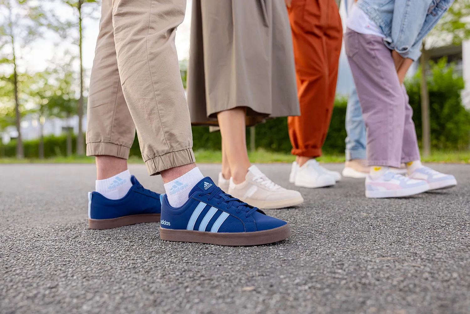 Eine Gruppe von Menschen läuft auf einer Straße und präsentiert verschiedene farbenfrohe Sneaker, darunter blaue, weiße und pastellfarbene Modelle.