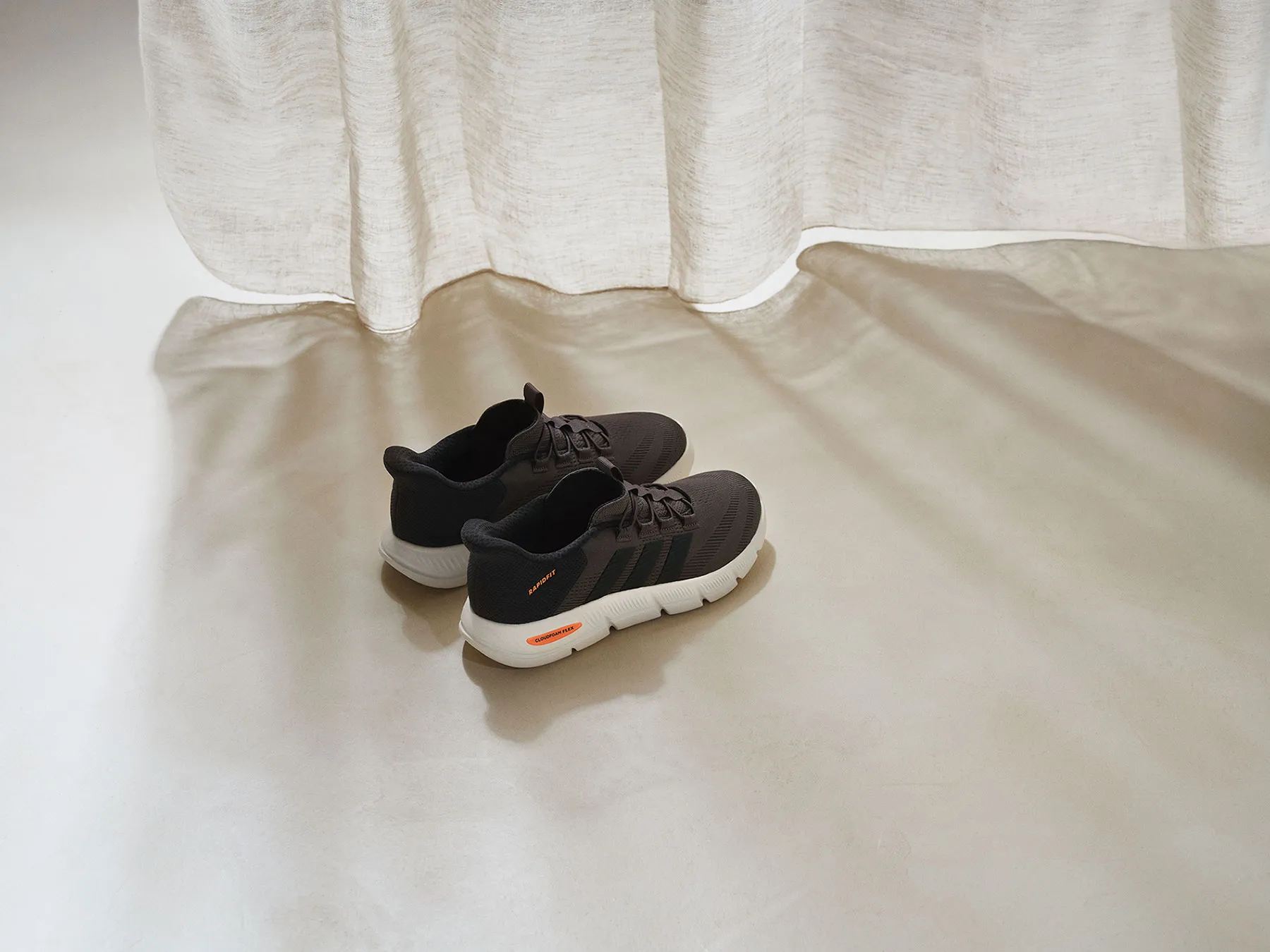 Graue adidas Cloudfoam-Sneaker stehen vor einem Vorhang.