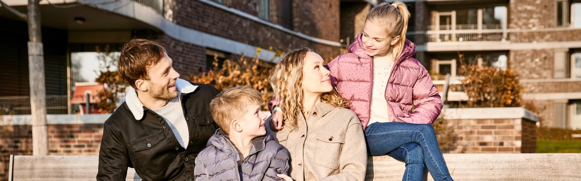 Eine Familie sitzt auf einer Bank und alle lächeln sich an.