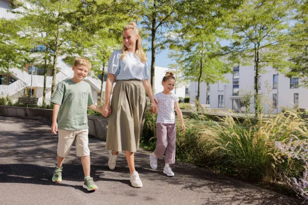 Eine Mutter geht mit zwei Kindern auf einem sonnigen Parkweg spazieren.