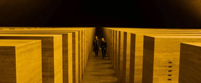 Two men walking along stone cubes covered in yellow light