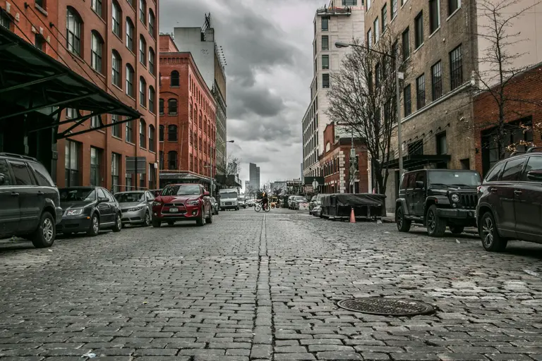 Cobblestone street with buildings and cars on either side