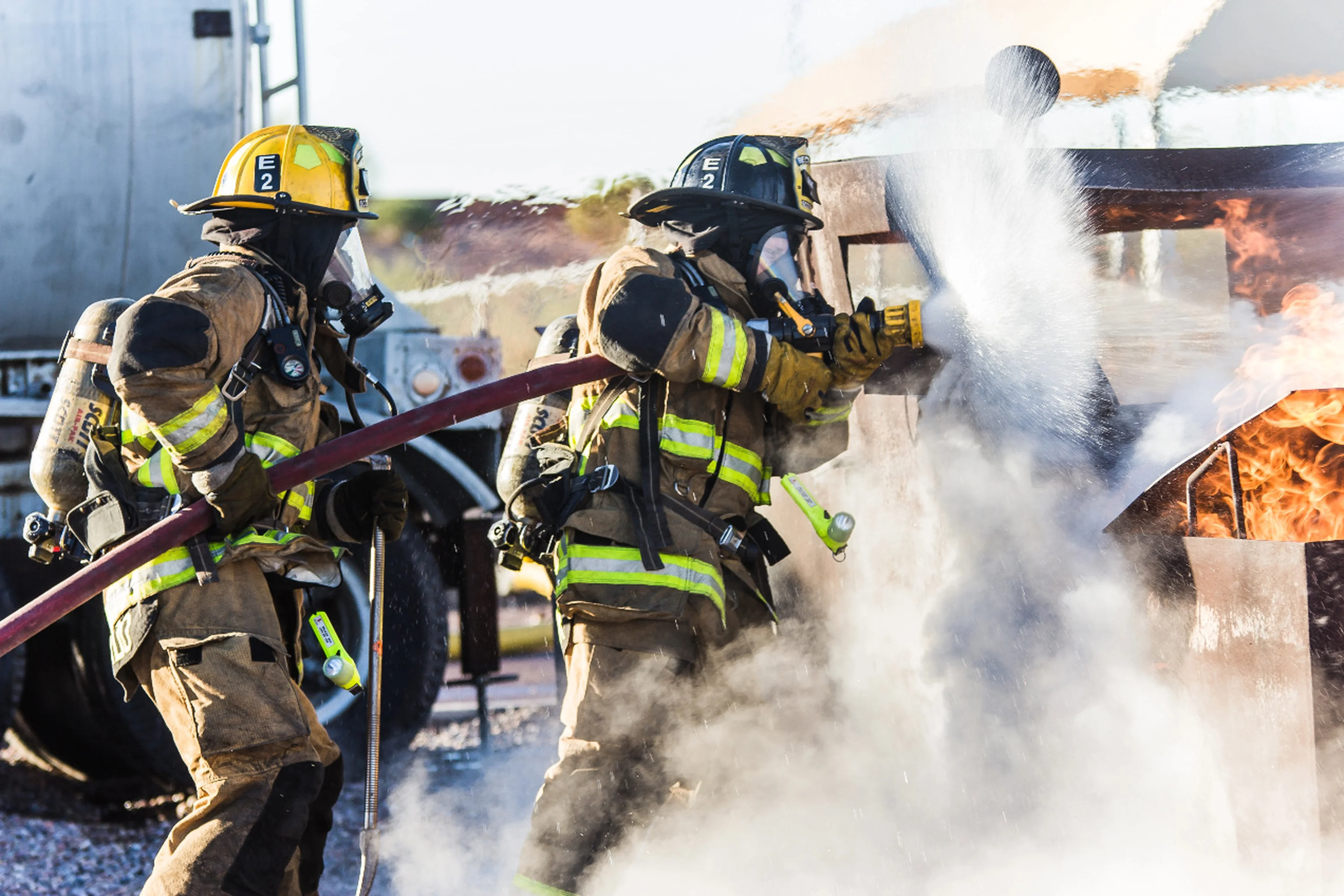 Two firefighters hold on to a hose that's spraying water on an active fire.