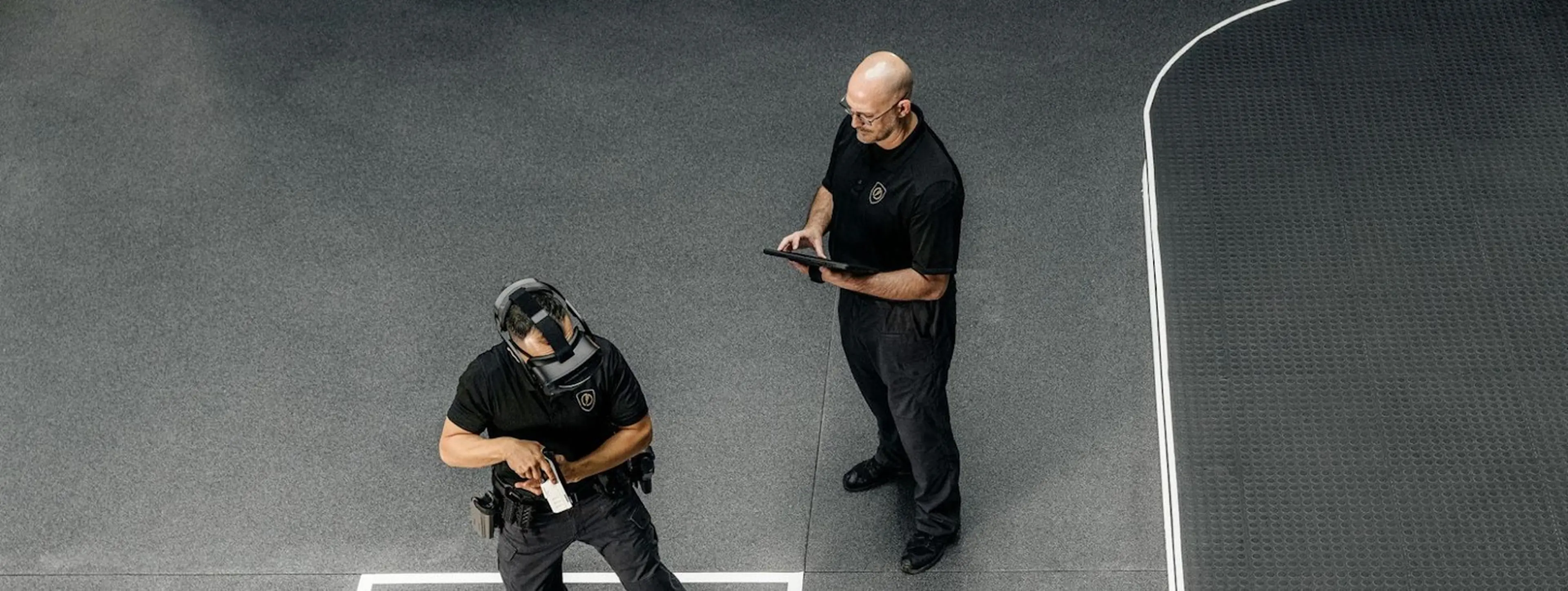 A law enforcement officer trains utilizing a virtual reality headset while a supervisor records his performance.