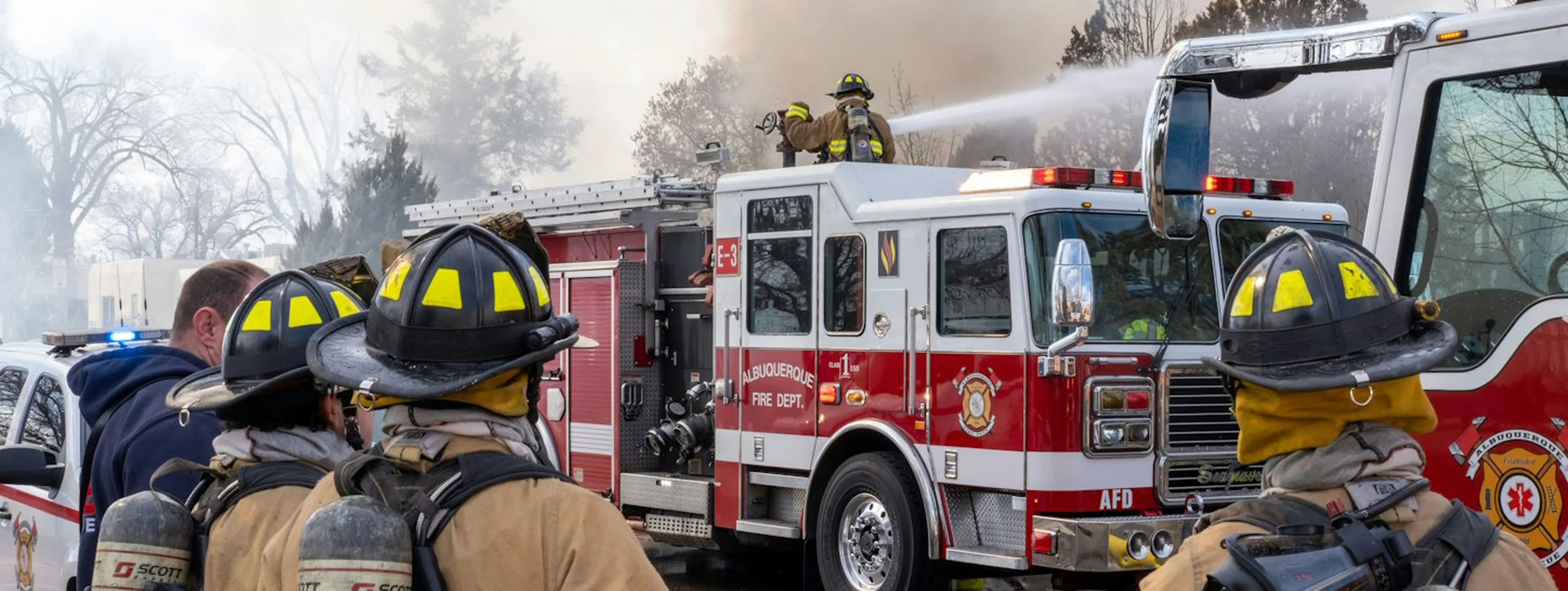 Firefighters in yellow helmets standing near a red firetruck in the daytime.