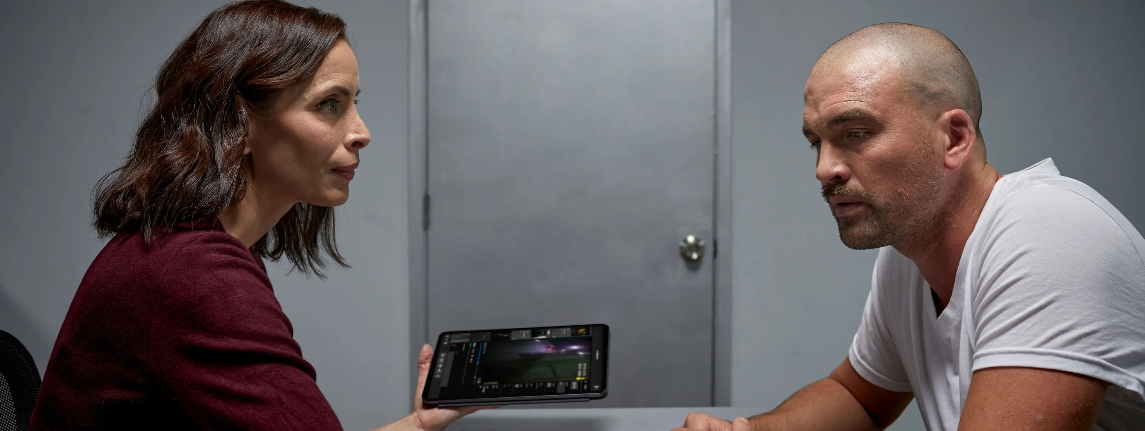 A lawyer meets with their client, showing them video evidence on a tablet.