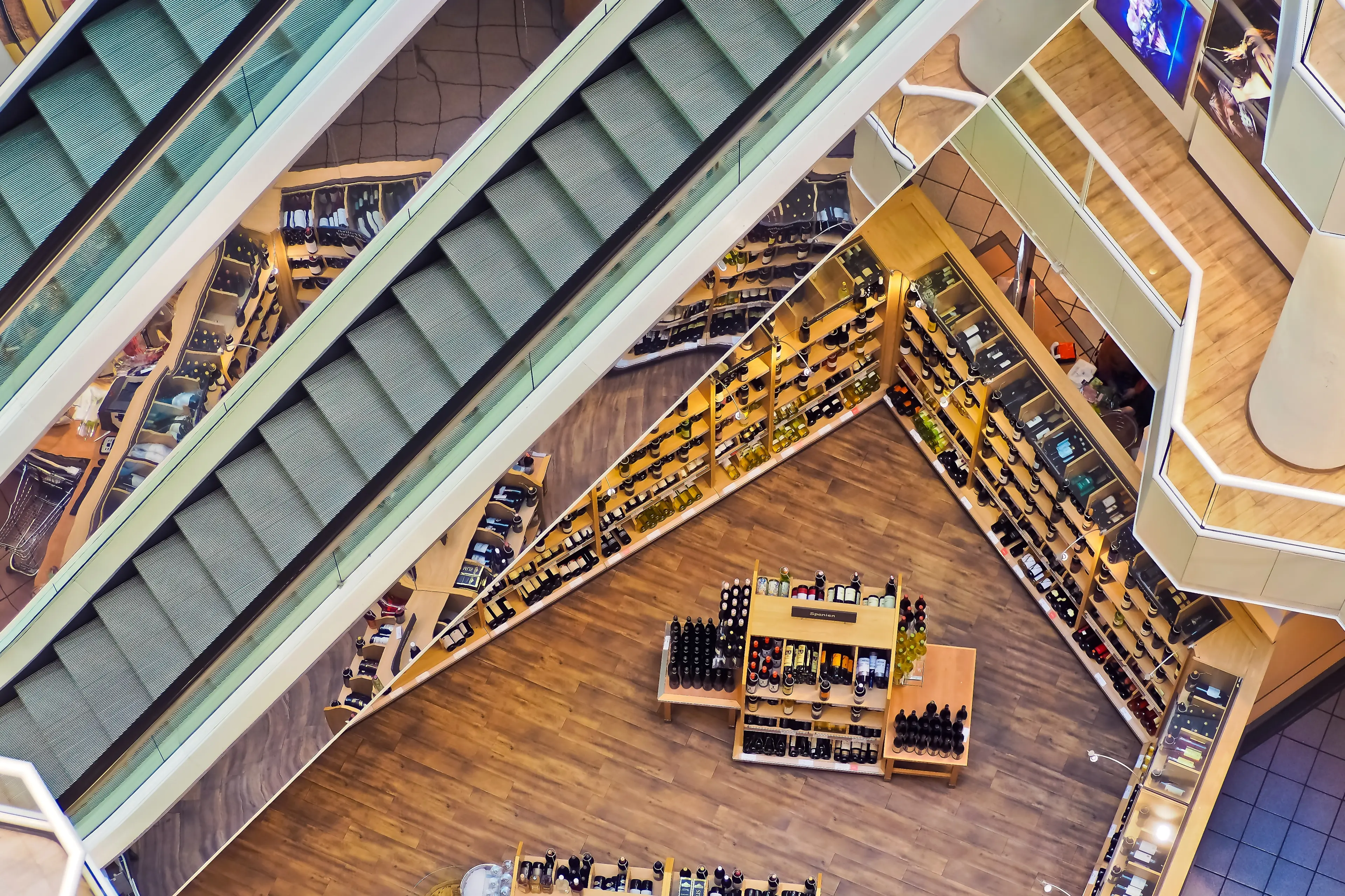 An array of wine shelves line the bottom floor of a multi-story shopping center.