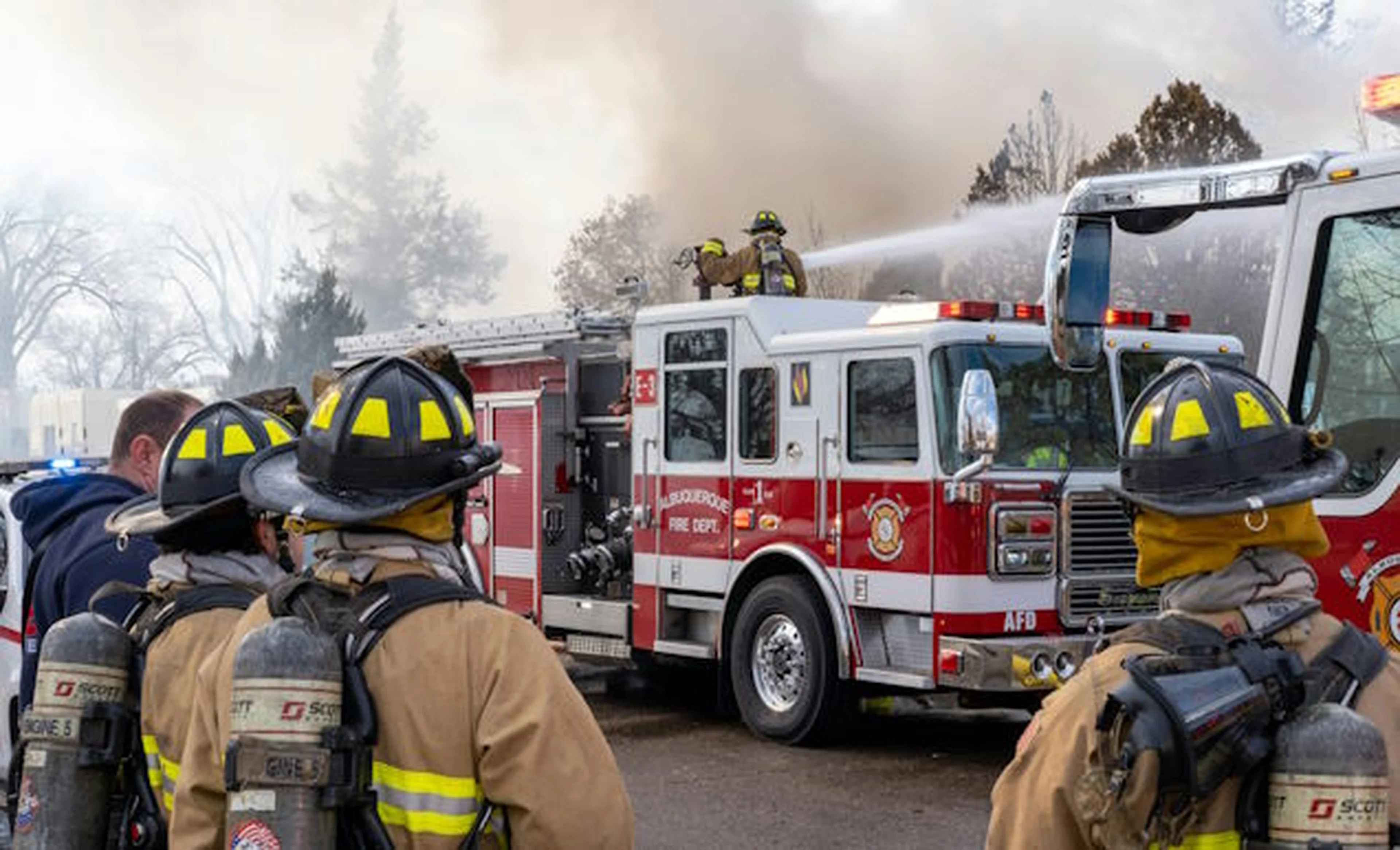 Firefighters in yellow helmets standing near a red firetruck in the daytime.