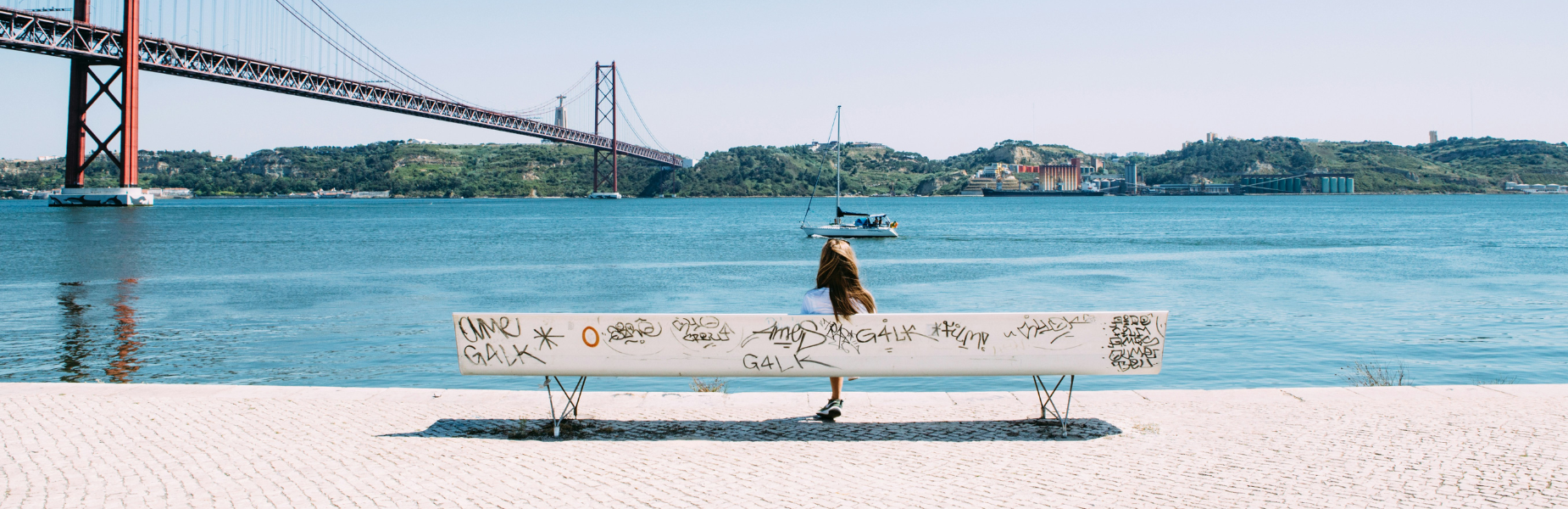 Meisje zit op een bankje uitkijkend op de brug in Lissabon