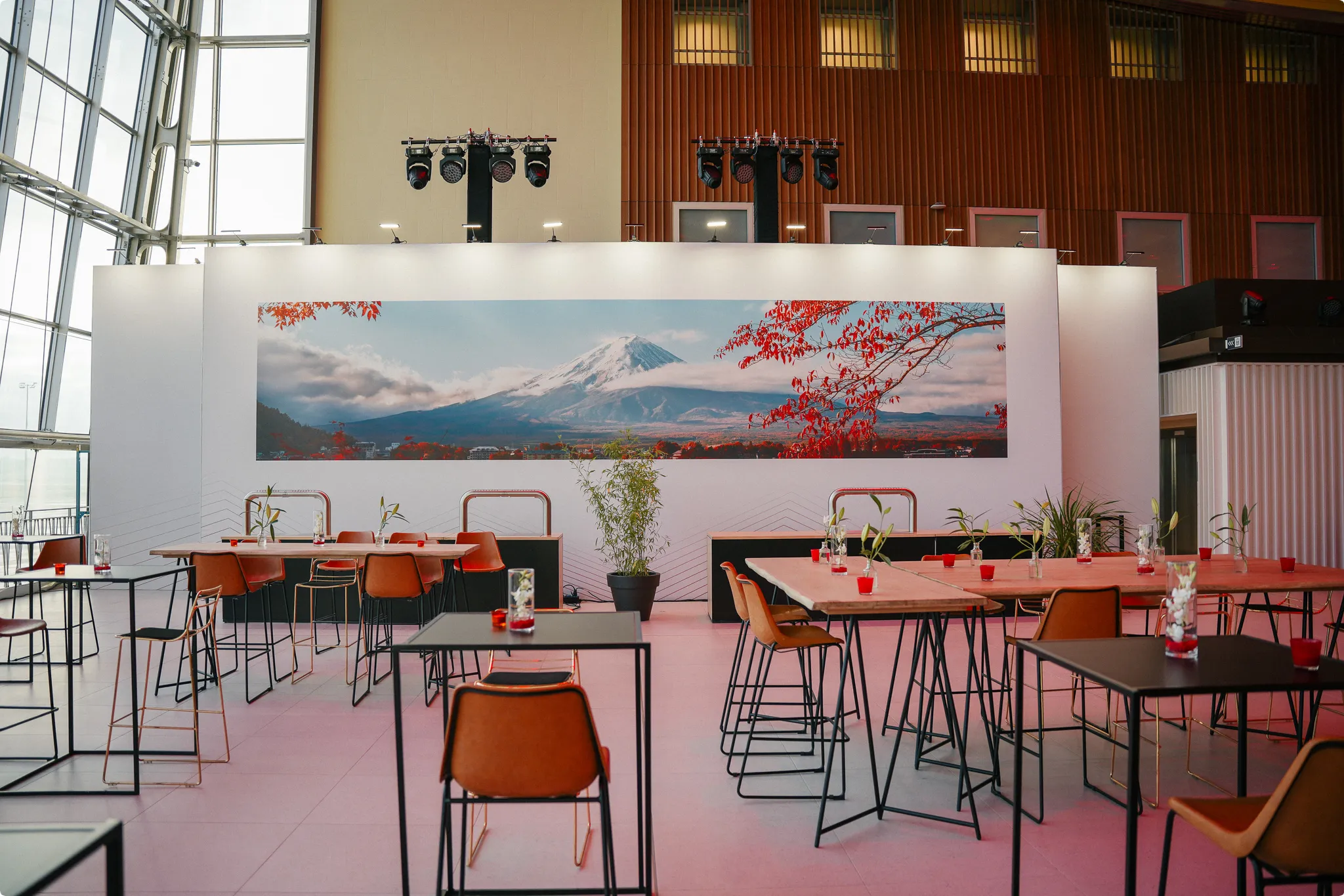 A modern dining area with tables and chairs, decorated with small plants. A large mural of a mountain and red leaves is on the wall.