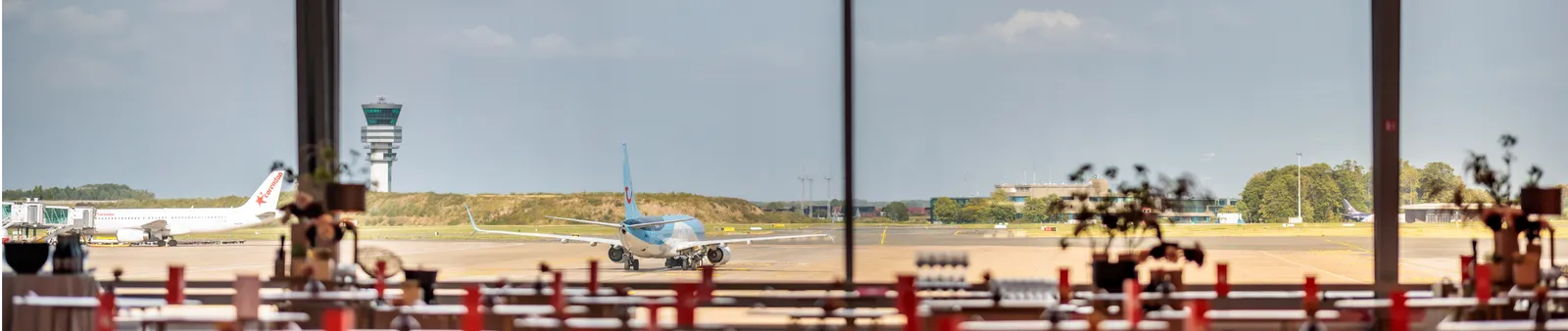 View from an airport lounge window showing two planes on the tarmac, a control tower, and a clear sky in the background.
