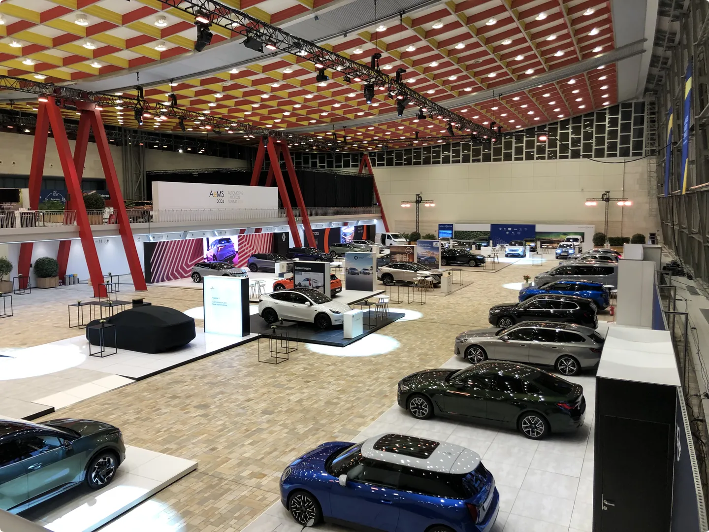 A spacious automotive exhibition hall with various cars on display, under a bright ceiling with red and yellow patterns.