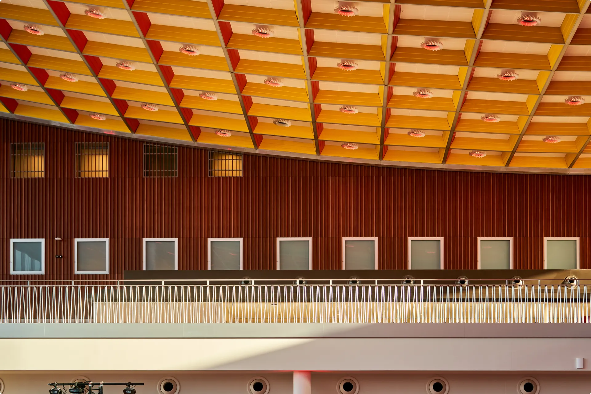 Interior view of a modern building with a geometric yellow and red patterned ceiling, wooden wall panels, and square windows.