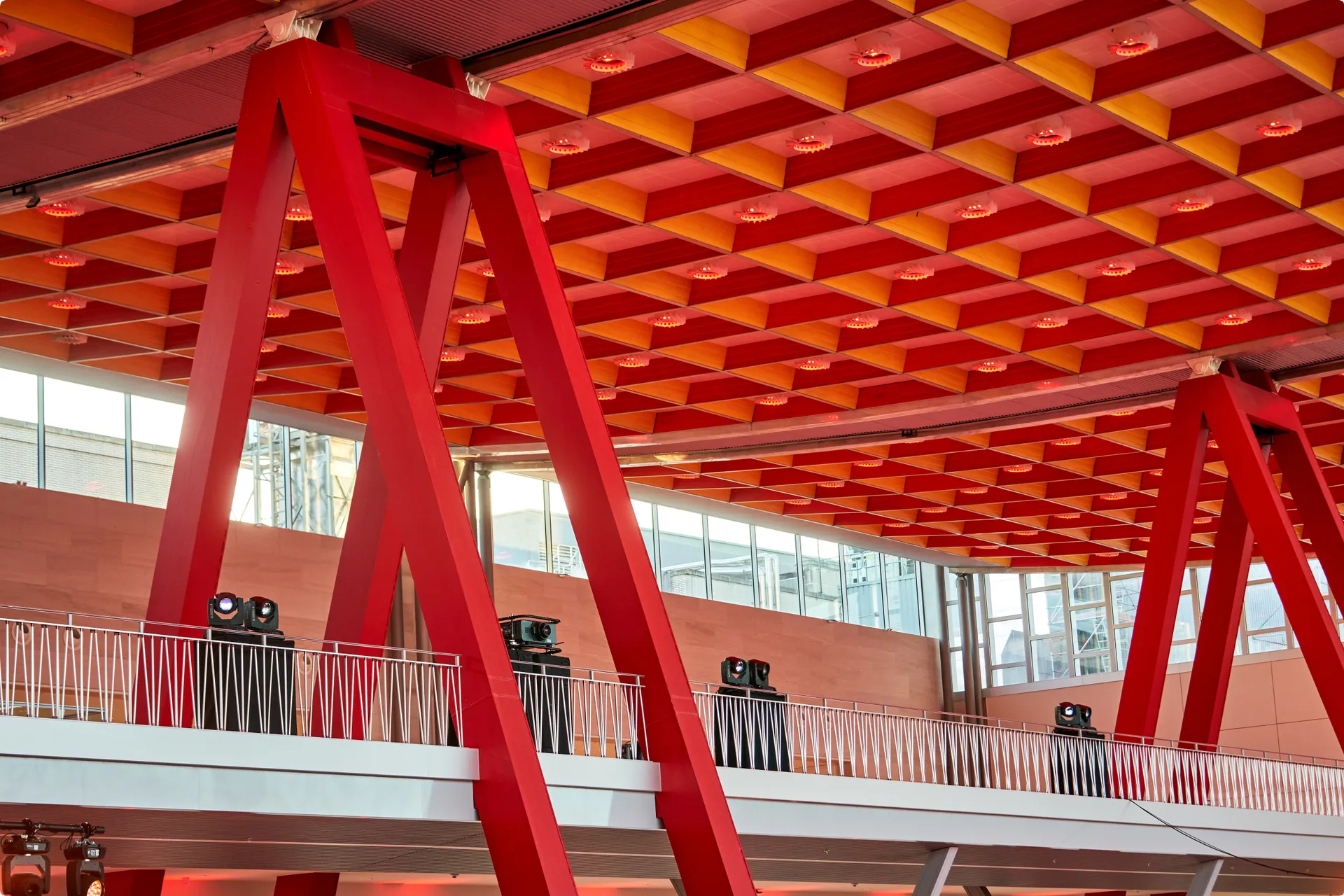 Interior with a geometric red ceiling, large red beams, and a metal railing in front of windows.