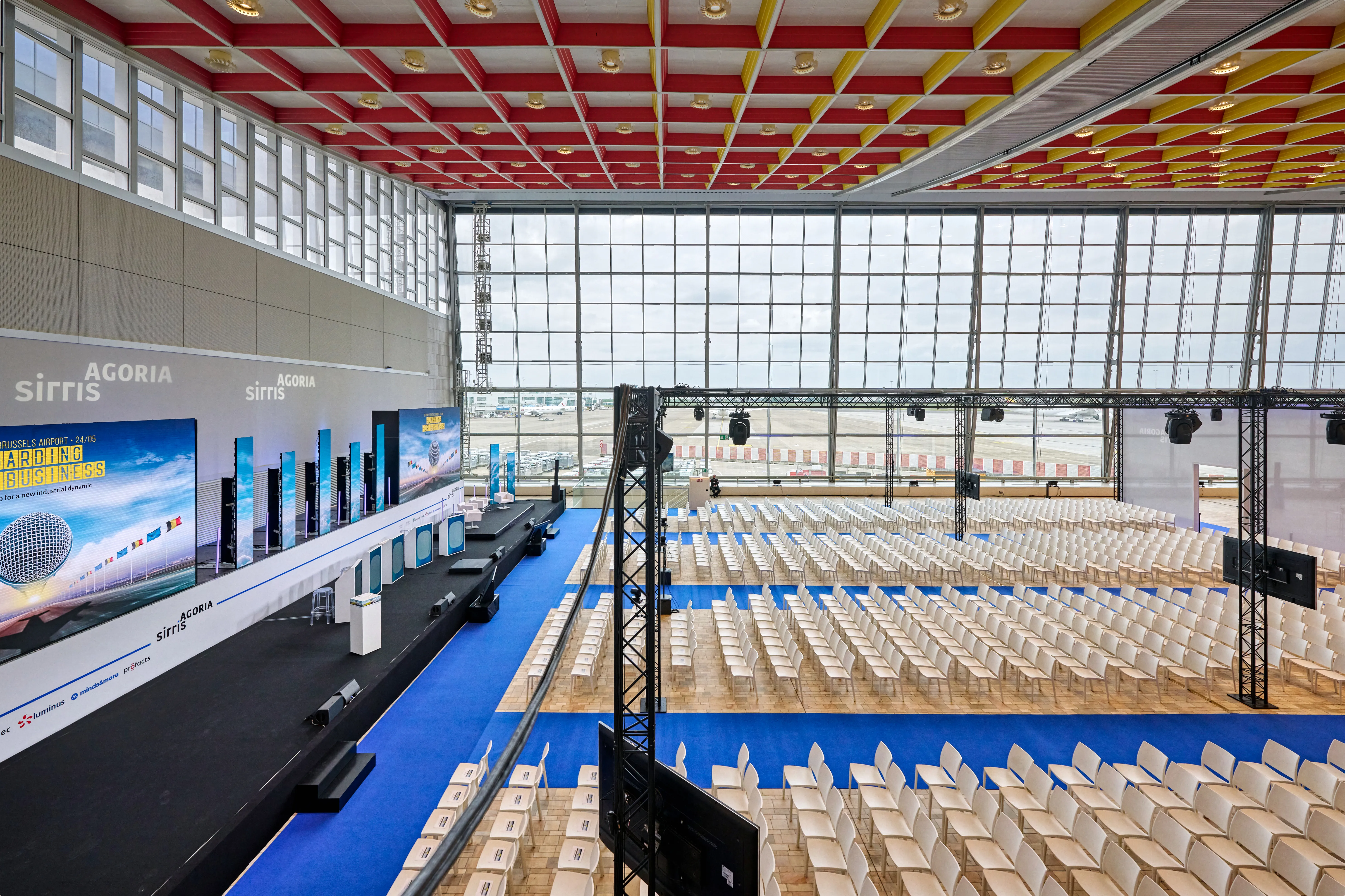 Large and spacious conference event set-up with big screen in front and large window with views on the tarmac on the side