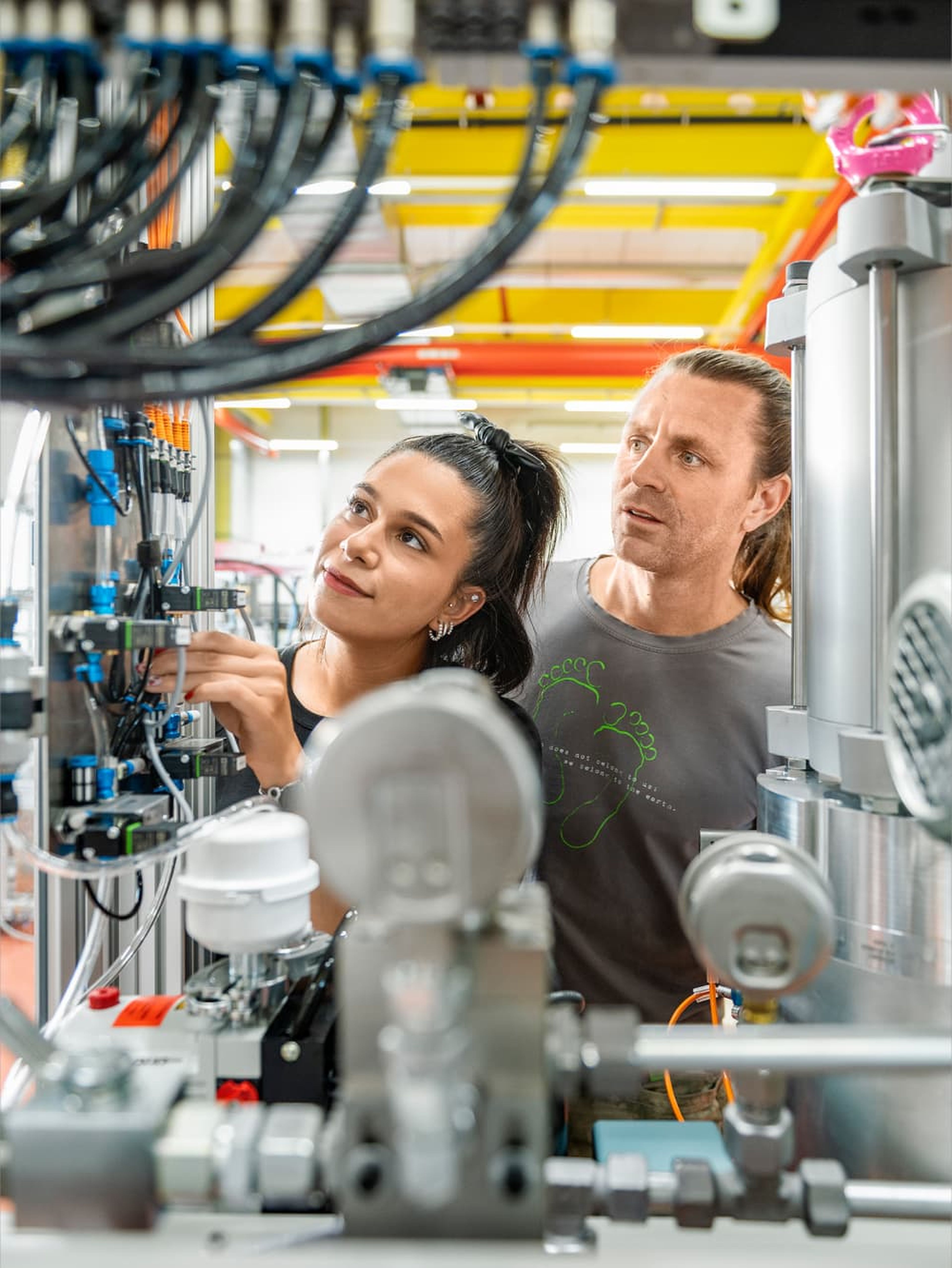Prozesstechnik Lehrling und Ausbilder schauen sich gemeinsam den Aufbau einer mechatronischen Anlage an. 