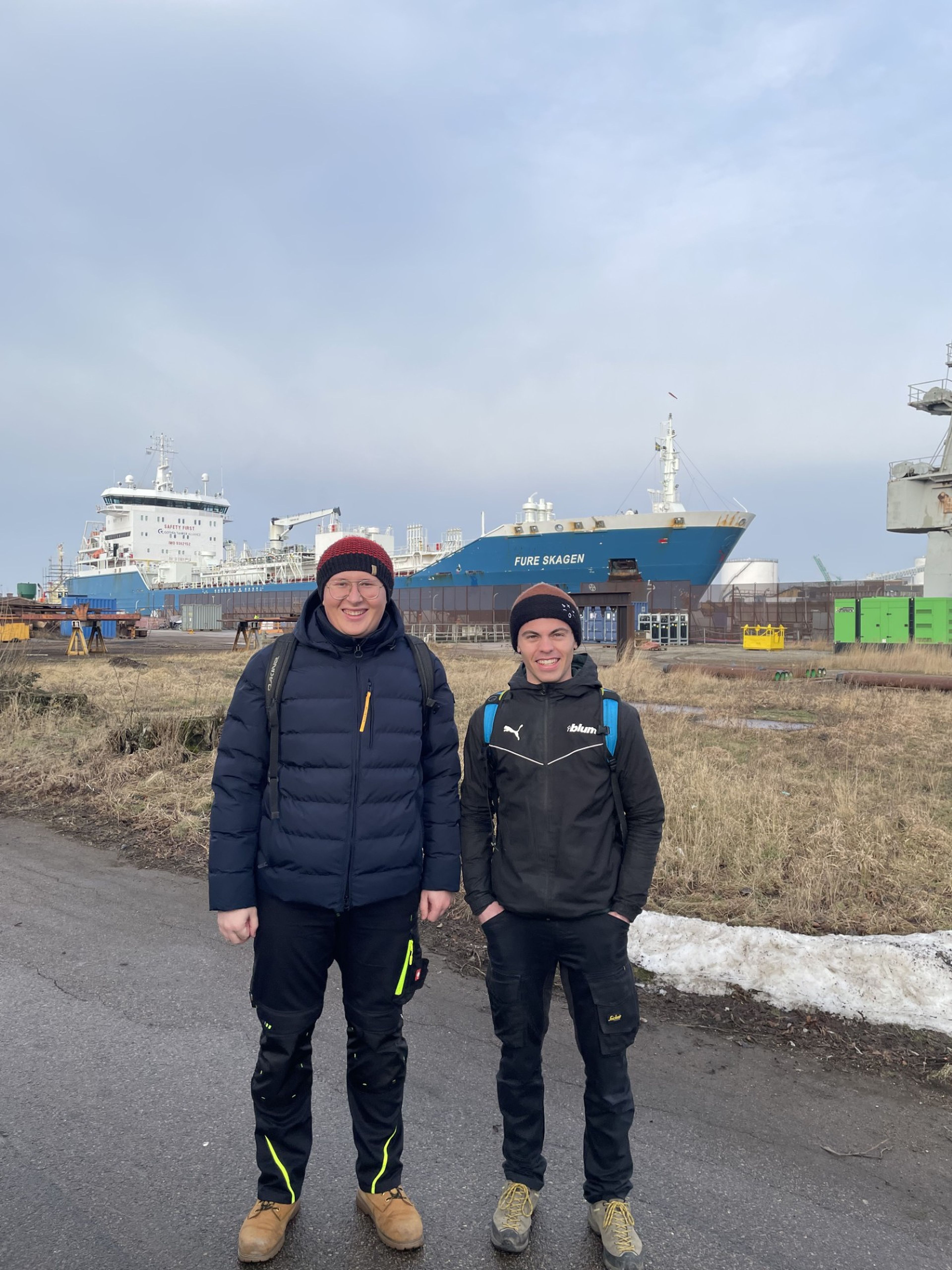Zwei Auszubildende im Bereich Mechatronik während ihres IFA-Auslandspraktikums in Lund, Schweden, stehen vor einem großen Frachtschiff im Hafen und sammeln internationale Berufserfahrung in der technischen Ausbildung bei Blum