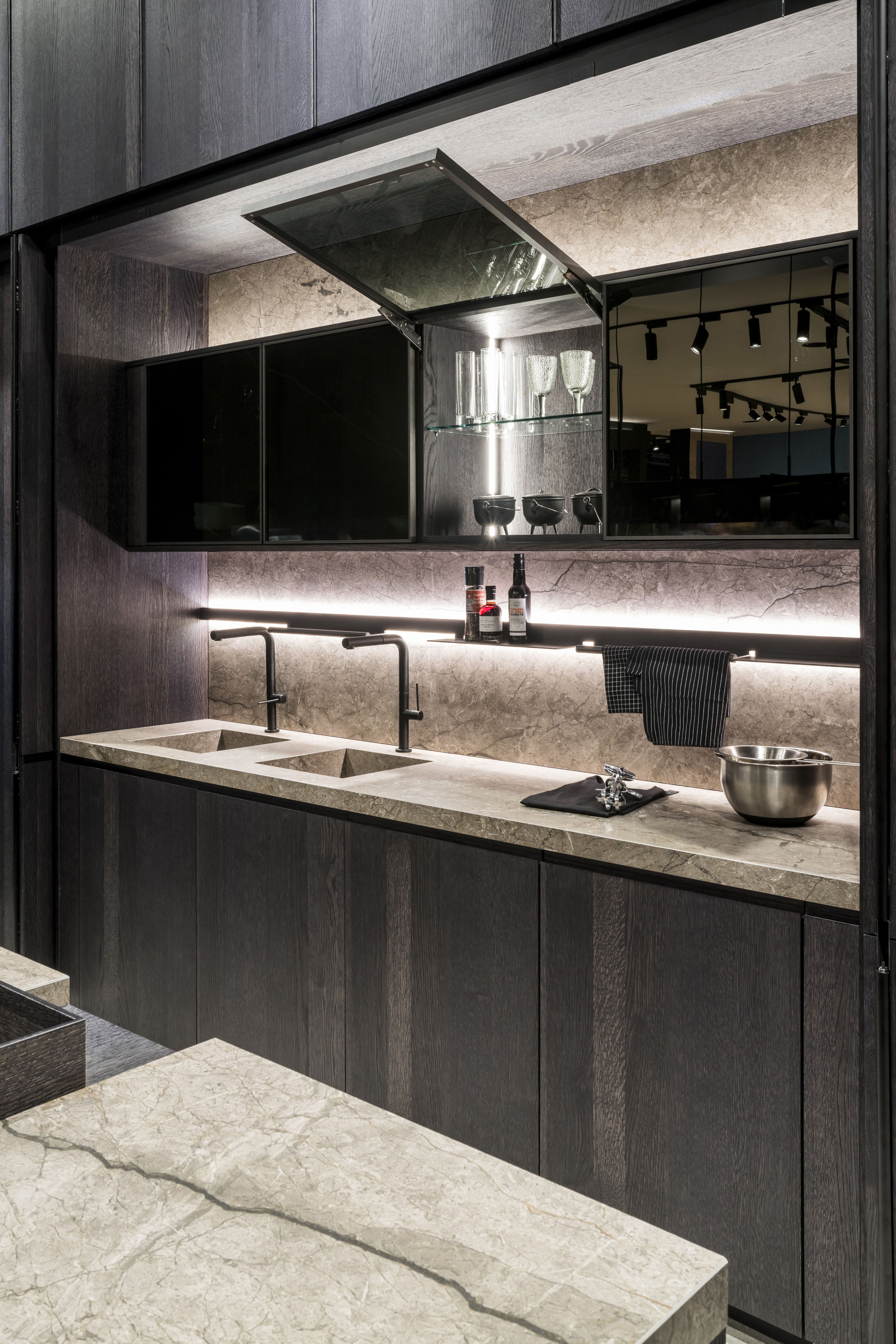 An open glass front with the AVENTOS HKi lift system in a dark-coloured kitchen