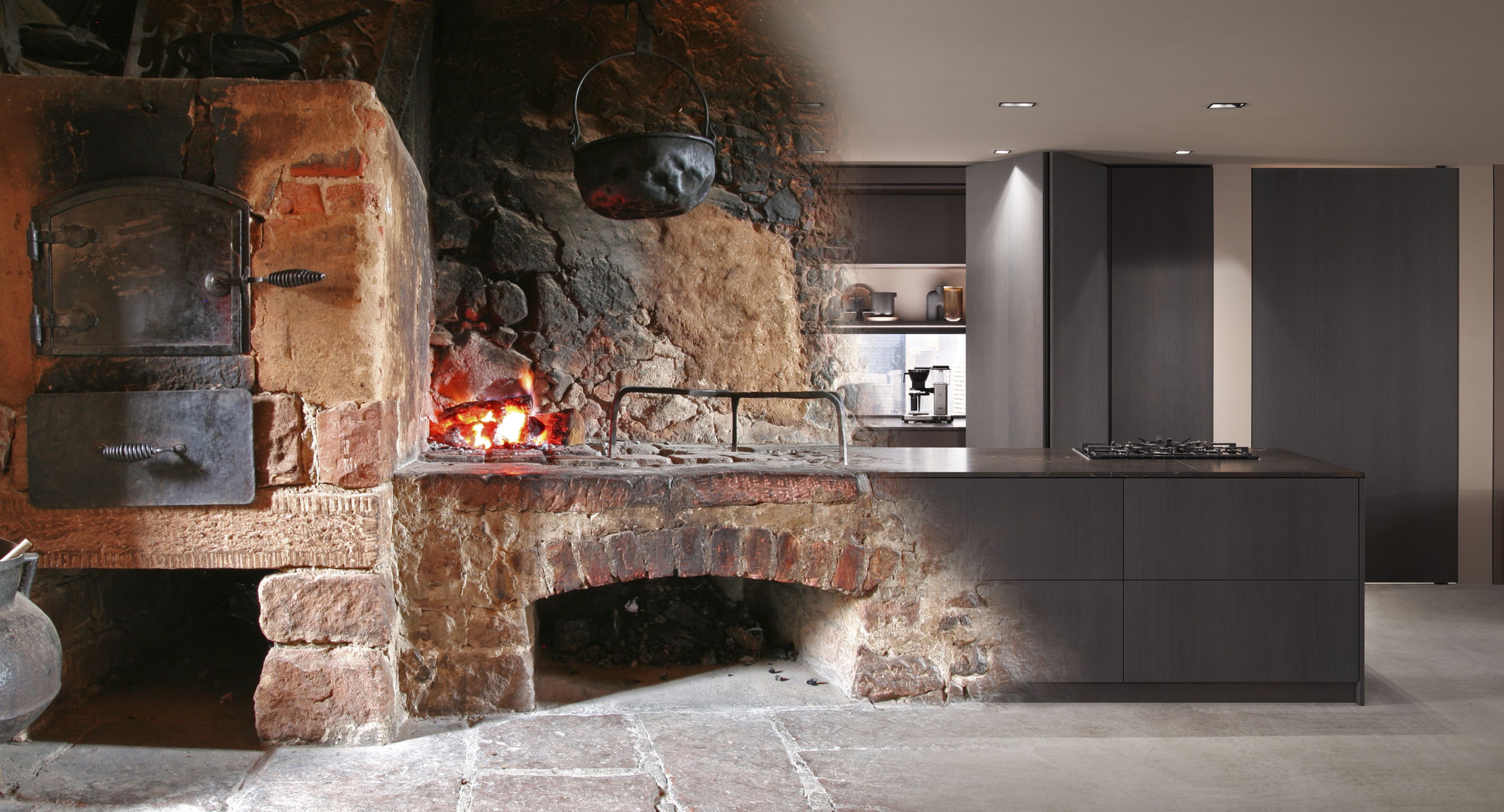A kitchen blending rustic and modern styles, featuring a traditional stone hearth with fire on one side and sleek cabinetry on the other.