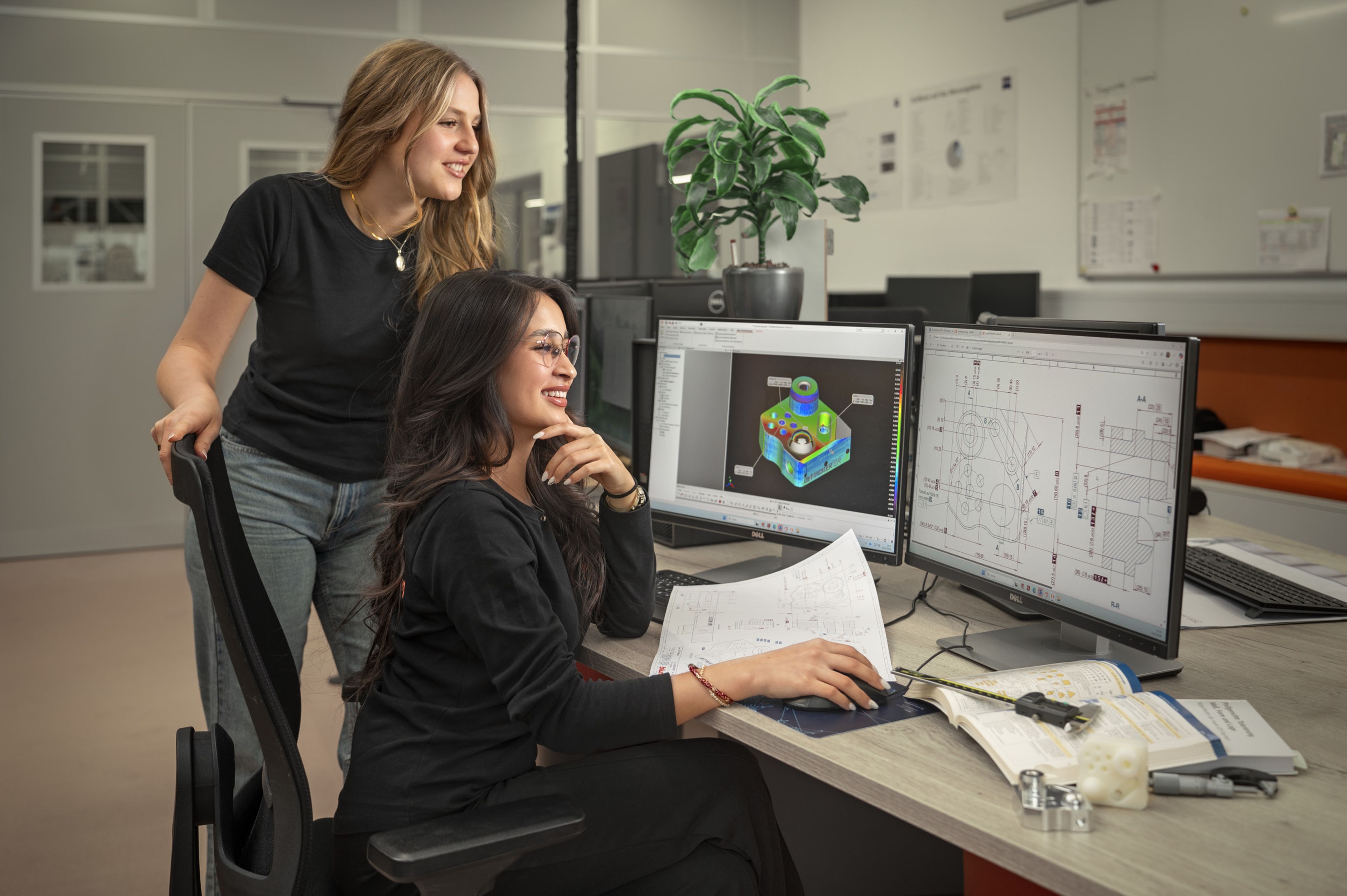 Auszubildende der Ausbildung bei Blum in der Fertigungsmesstechnik analysieren ein Bauteil am Computerarbeitsplatz mit CAD‑Modell, technischer Zeichnung und Messprotokollen in einer modernen Arbeitsumgebung.