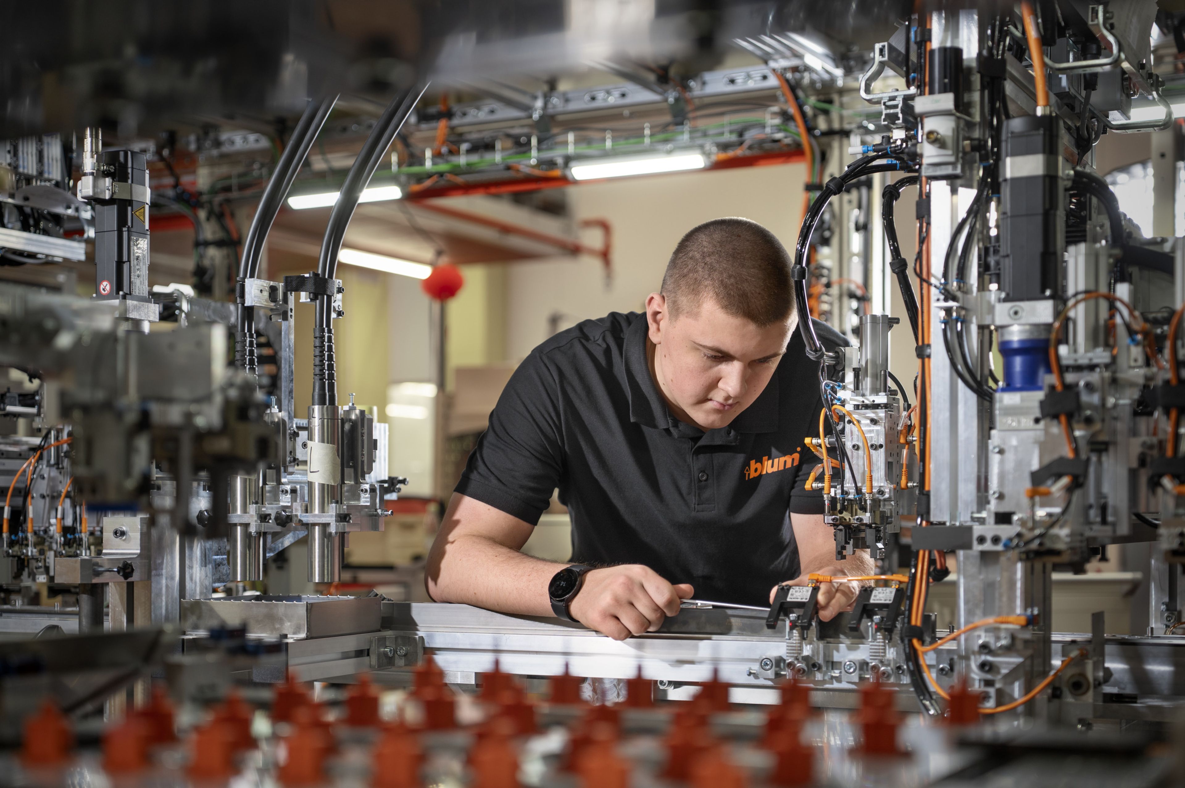 Ein Auszubildender führt in einer Produktionsanlage präzise mechanische Montage‑ und Prüfarbeiten an Maschinenkomponenten durch, um die korrekte Funktion der Anlage sicherzustellen