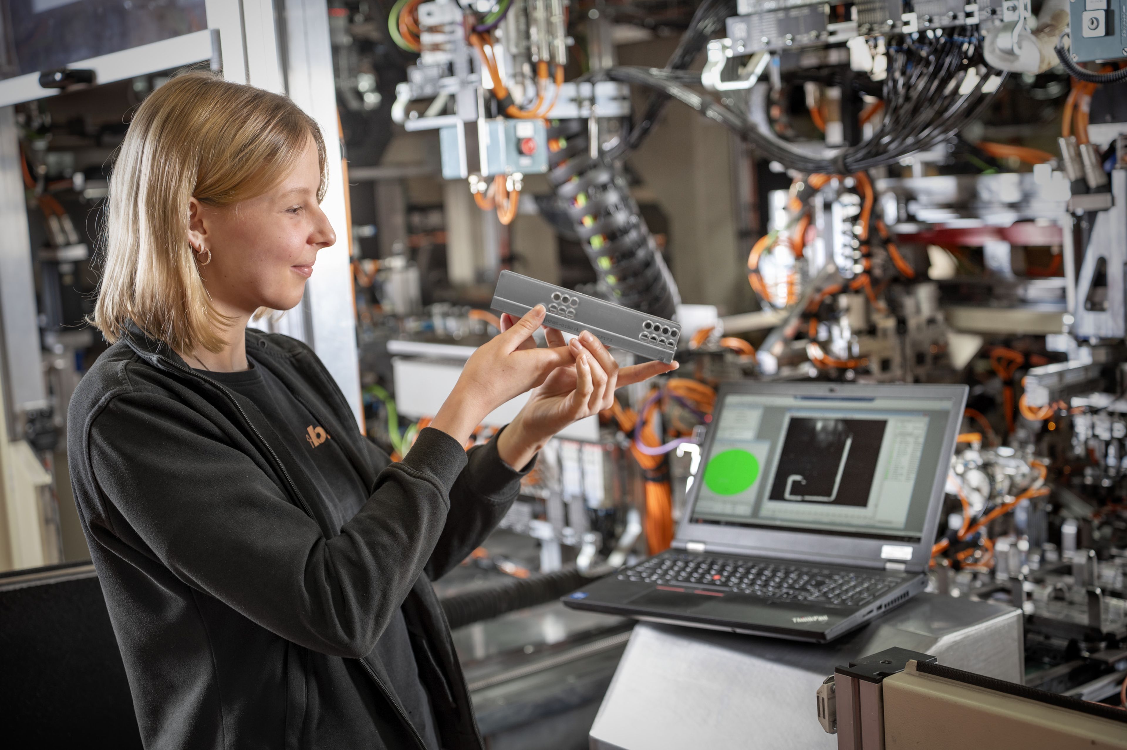 Trainee überprüft und repariert eine industrielle Kameratechnik im Anlagenverbund, analysiert Bilddaten am Laptop und prüft die Funktion der sensorgestützten Qualitätskontrolle.