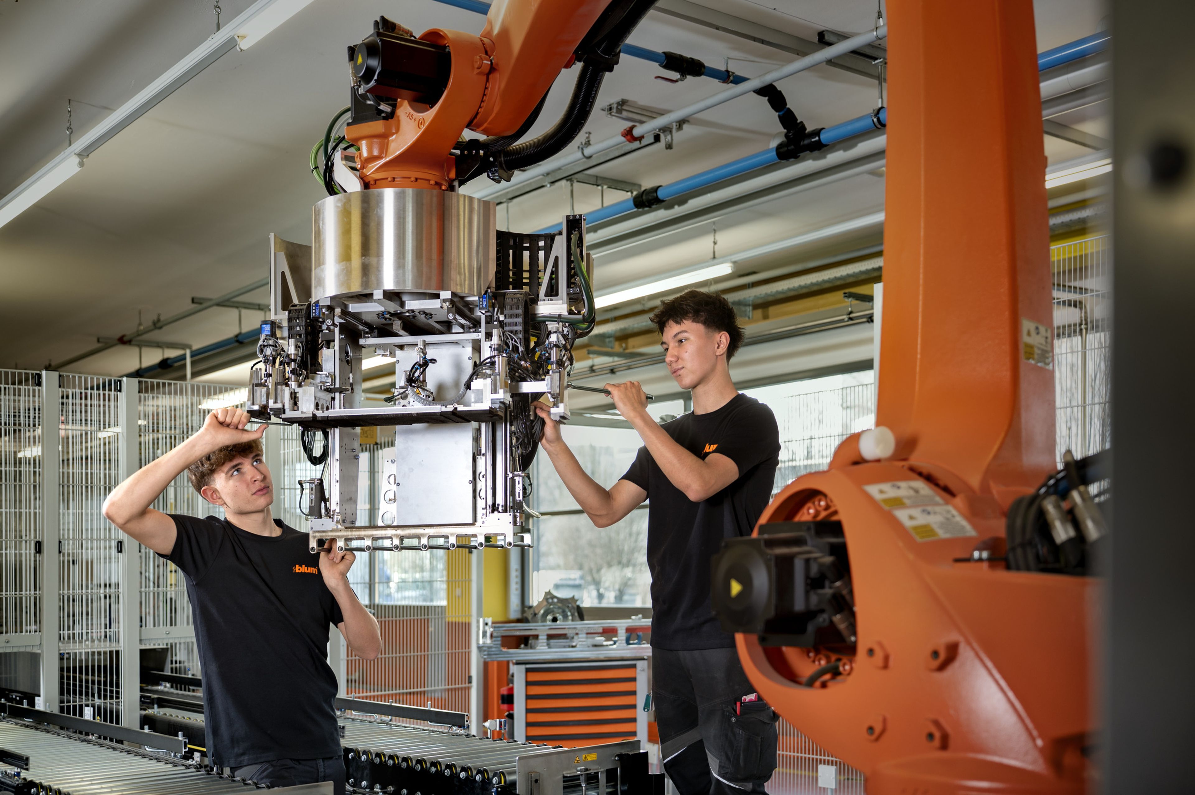 Auszubildende in der Maschinenbautechnik arbeiten praktisch an einem großen Industrieroboterarm und montieren Bauteile durch Verschrauben direkt an der automatisierten Anlage.