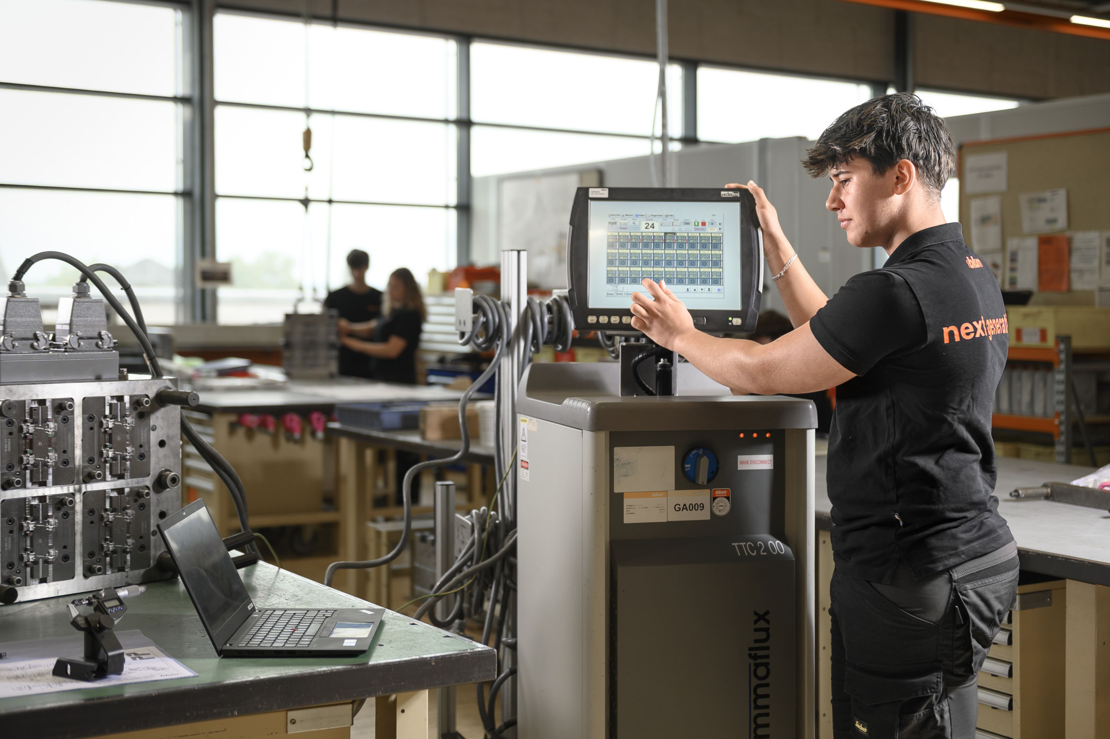 Lehrling der Werkzeugbautechnik bei Blum arbeitet mit einem Gammaflux-Heißkanalsystem zur Steuerung eines Spritzgusswerkzeugs. Die Ausbildung umfasst Prozessoptimierung, Projektmanagement sowie die Herstellung, Wartung und Optimierung von Stanz-, Spritzguss- und Druckgusswerkzeugen.