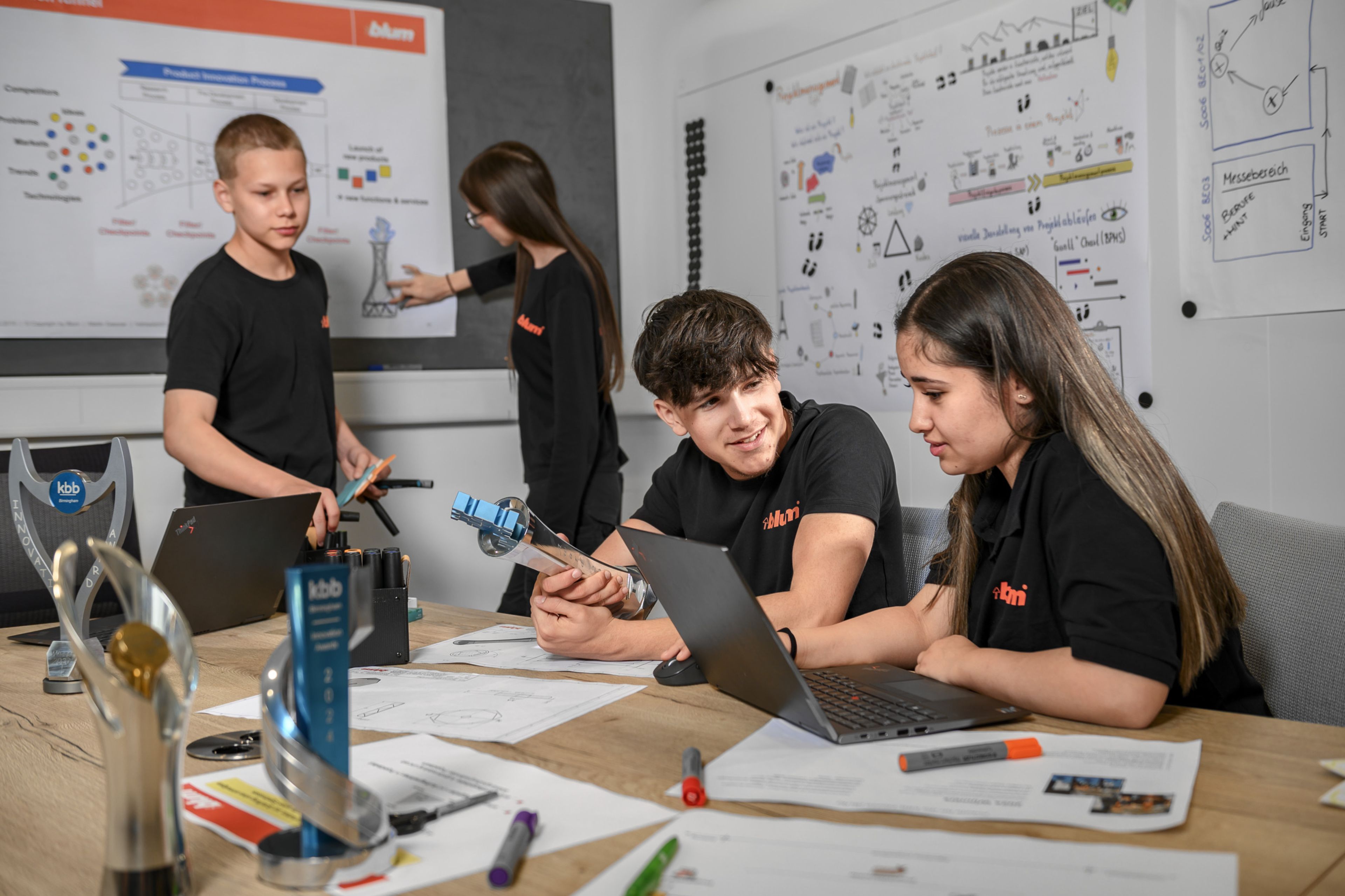 Mehrere Auszubildende bei Blum arbeiten im Rahmen eines technischen Projekts gemeinsam an der Planung, Entwicklung und Präsentation von Fertigungsbauteilen. Das Bild zeigt Projektmanagement in der Zerspanungstechnik mit Teamarbeit, digitaler Zusammenarbeit, technischen Zeichnungen und Visualisierungen sowie die praxisnahe Ausbildung bei Blum.