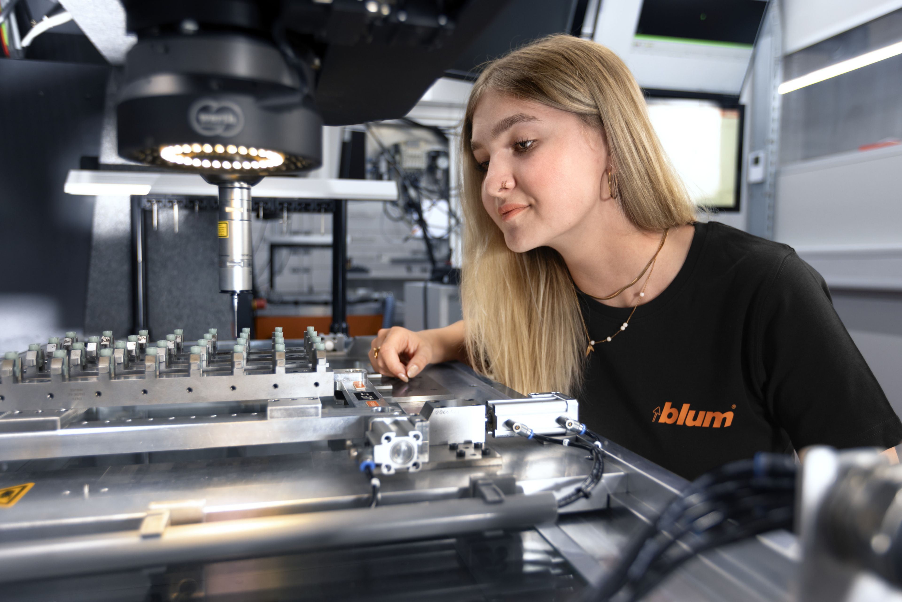 Das Bild zeigt einen Lehrling der Fertigungsmesstechnik, die gerade ein Bauteil mit einer Hightech-Messmaschine ausmisst. 