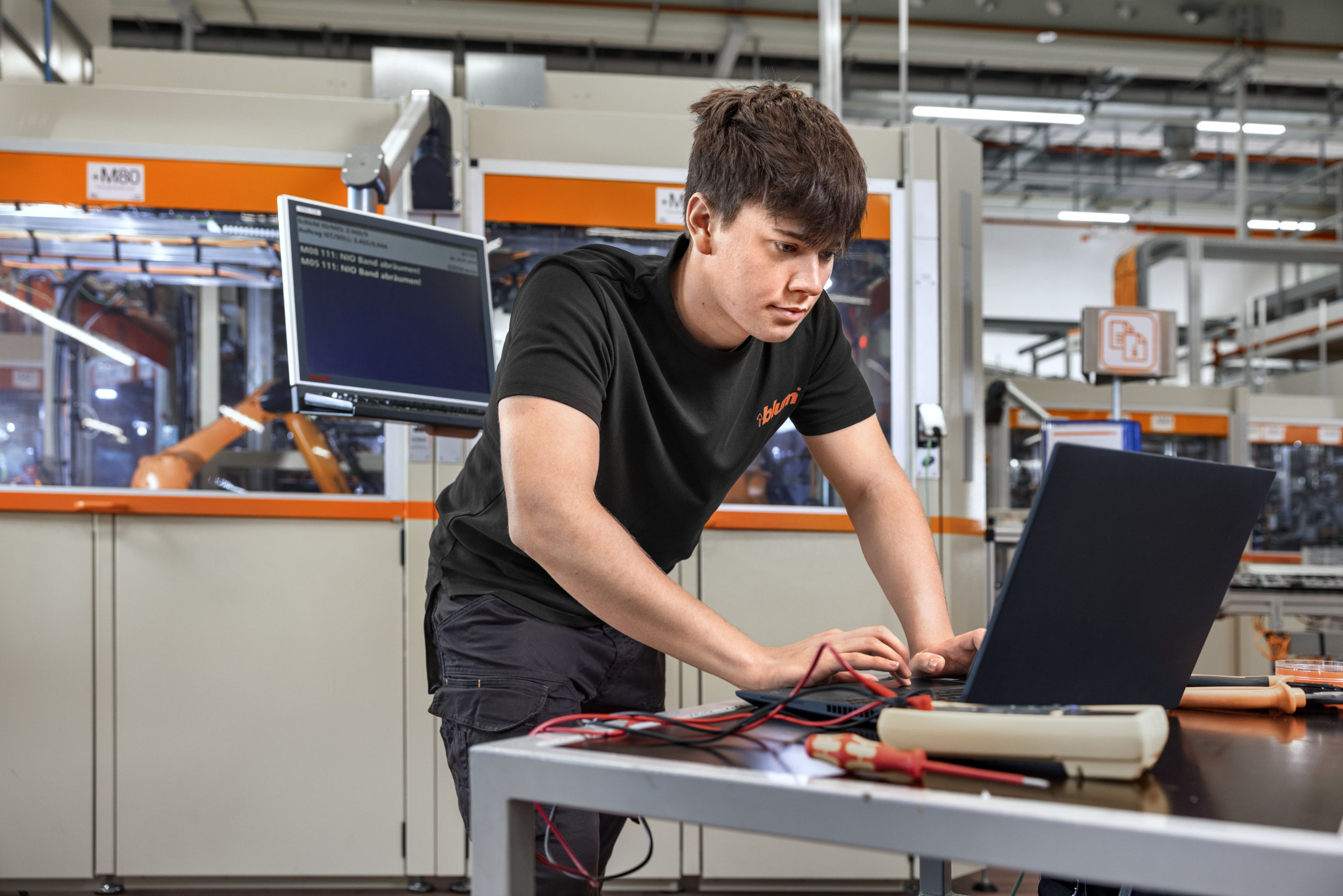 Das Foto zeigt einen Elektrotechnik-Lehrling der gerade eine Fehlersuche an einer Hightech-Anlage durchführt. 